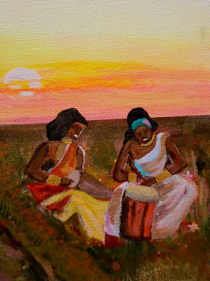 Two women drumming in a field at sunset